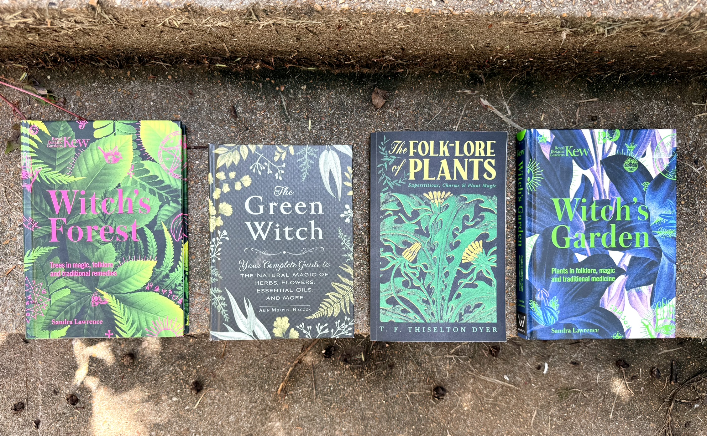 Four botanical and folklore books laid out on a stone step — the apothecary reading list