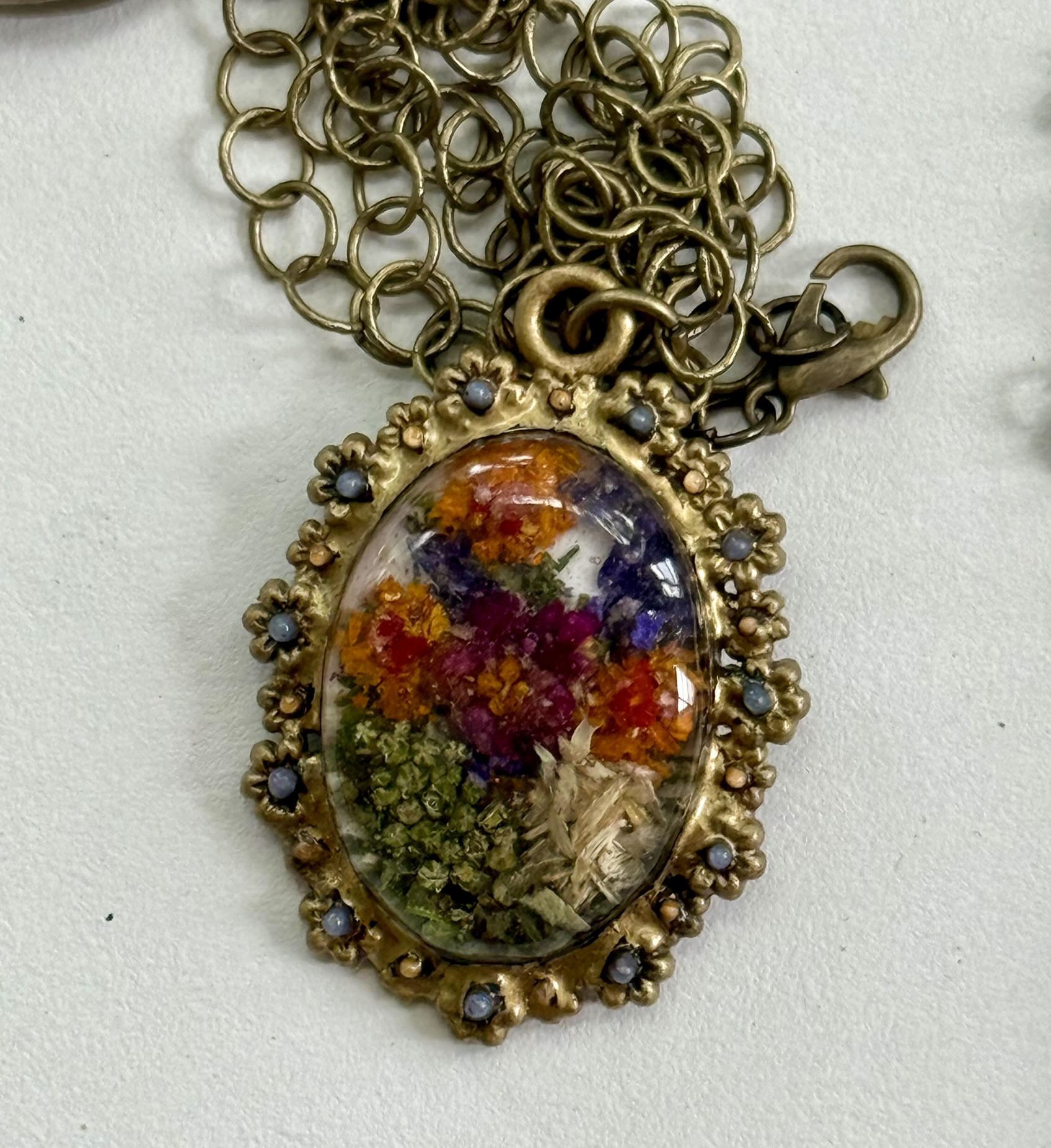 Ornate oval pendant filled with pixelated petals in orange, purple, crimson, and green
