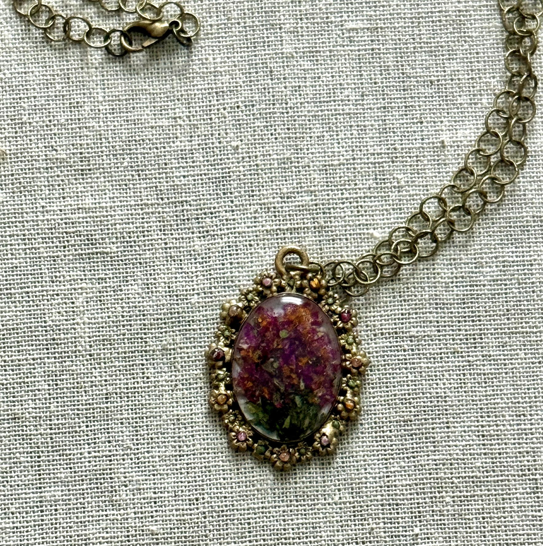 Ornate oval pendant on silver chain, deep crimson pixelated petals in an ornate bezel