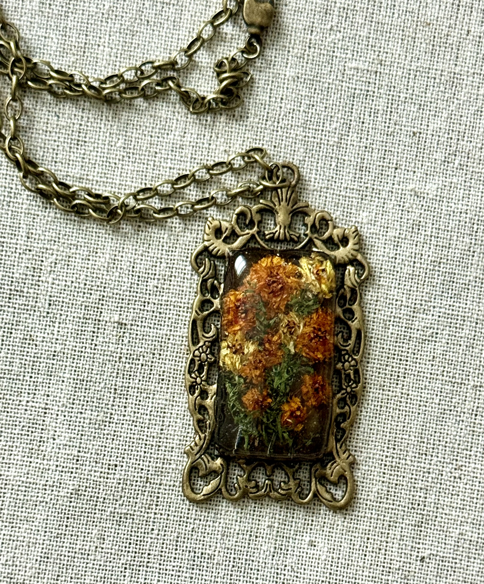 Rectangular pendant in ornate brass frame, amber and gold pixelated petals suggesting a sunflower
