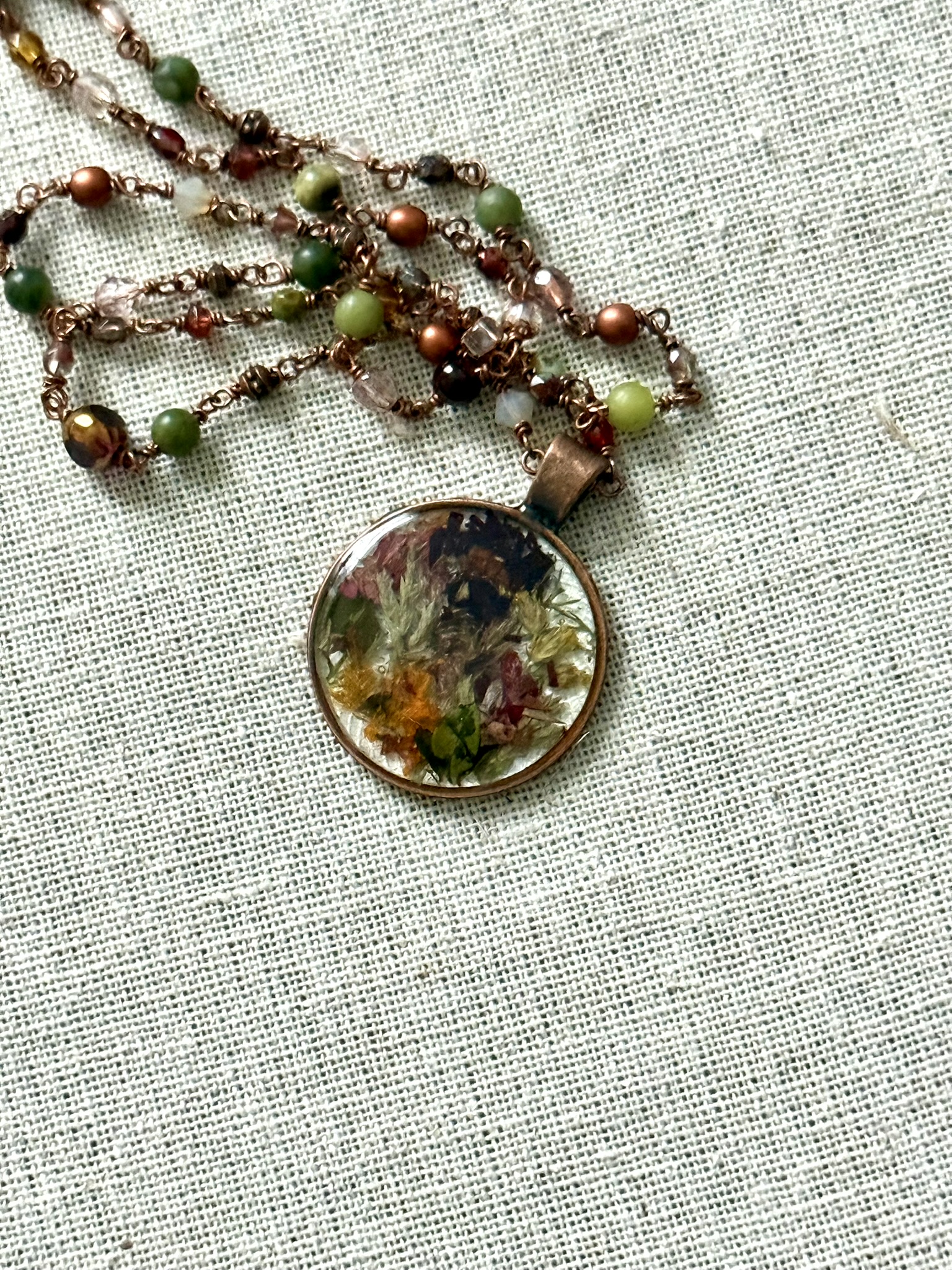Round pendant on a beaded copper necklace, earth-tone botanical pixel tiles