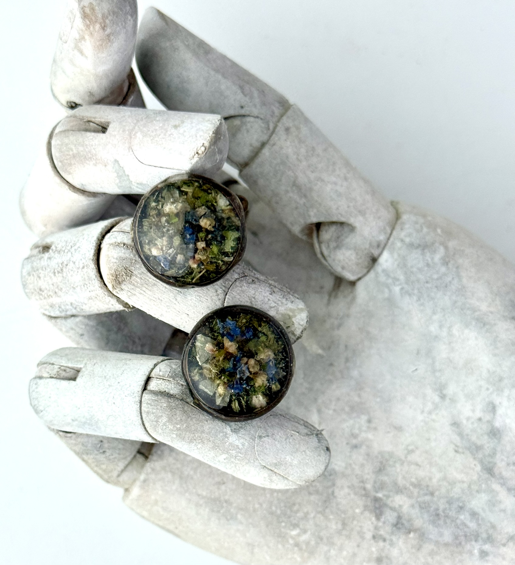 Two rings on a white wooden hand, green and blue botanical pixel tiles