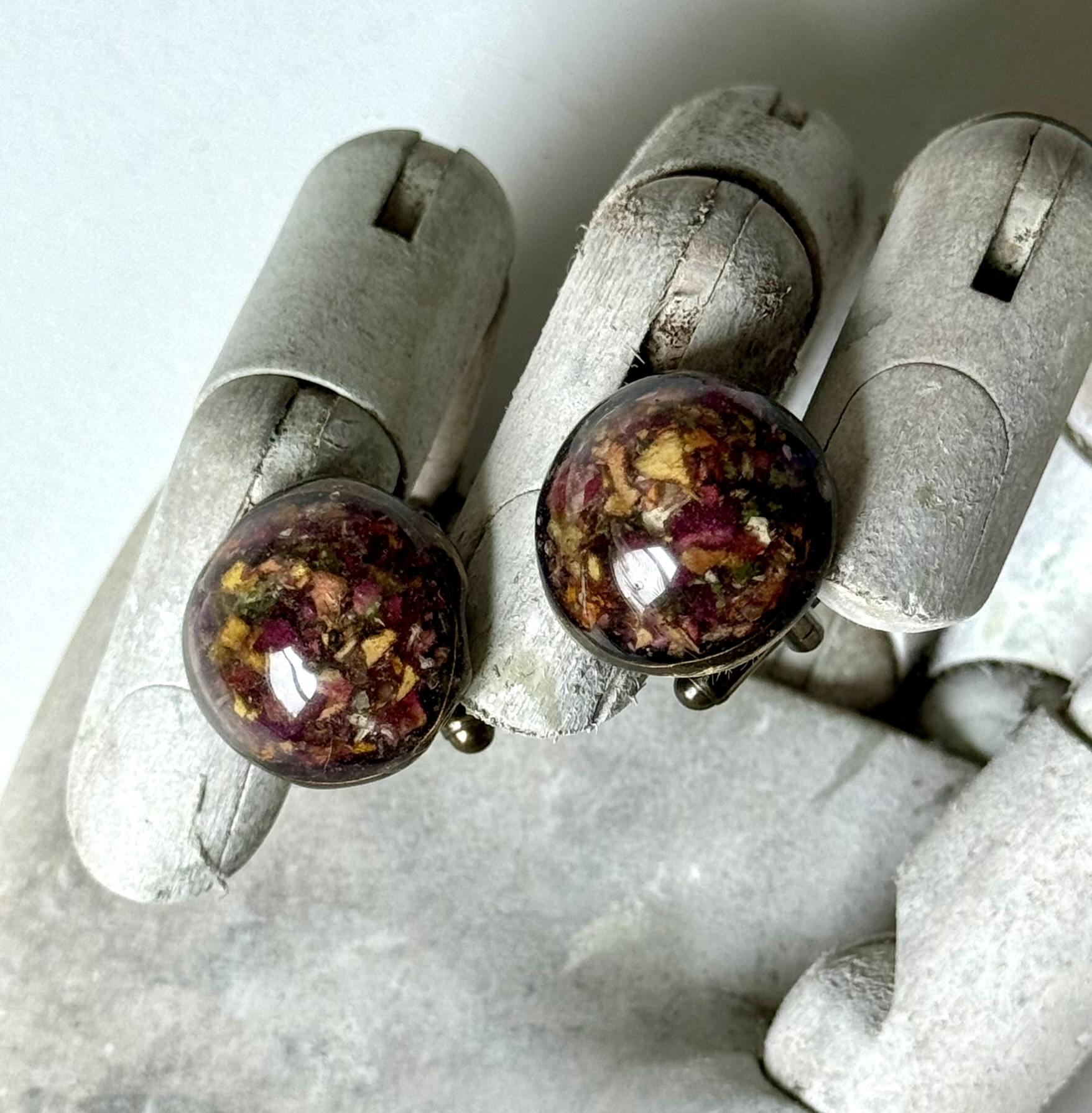Pair of dome stud earrings on a wooden hand, crimson and gold botanical pixels