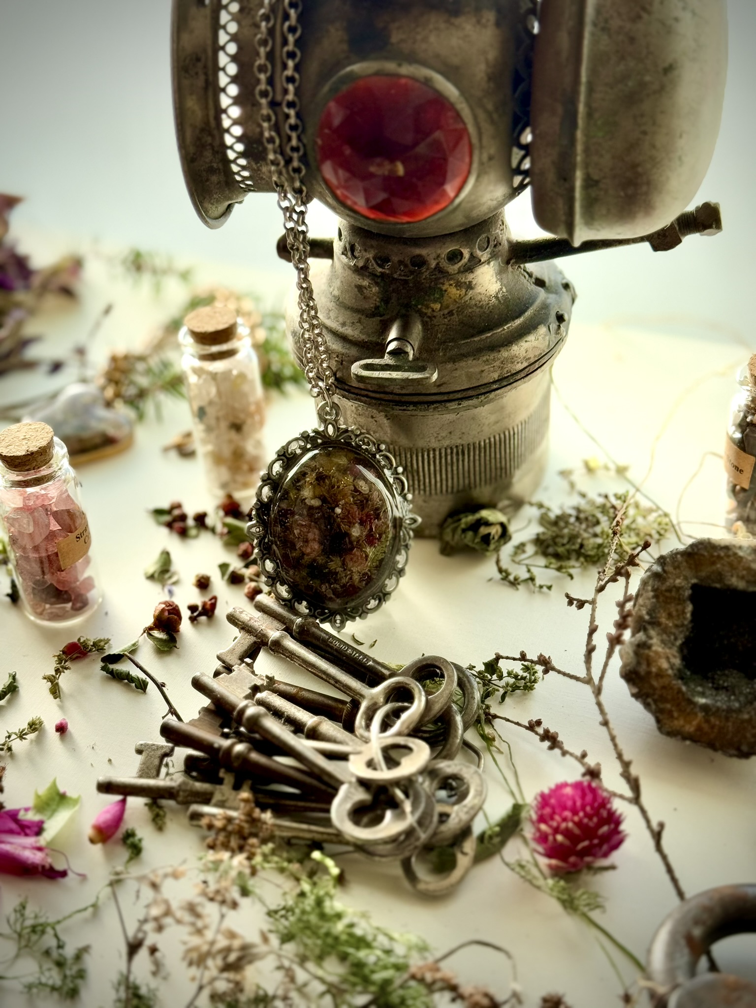 An antique lantern with red jewel glass, skeleton keys, and a botanical pendant — the studio as cabinet of curiosities