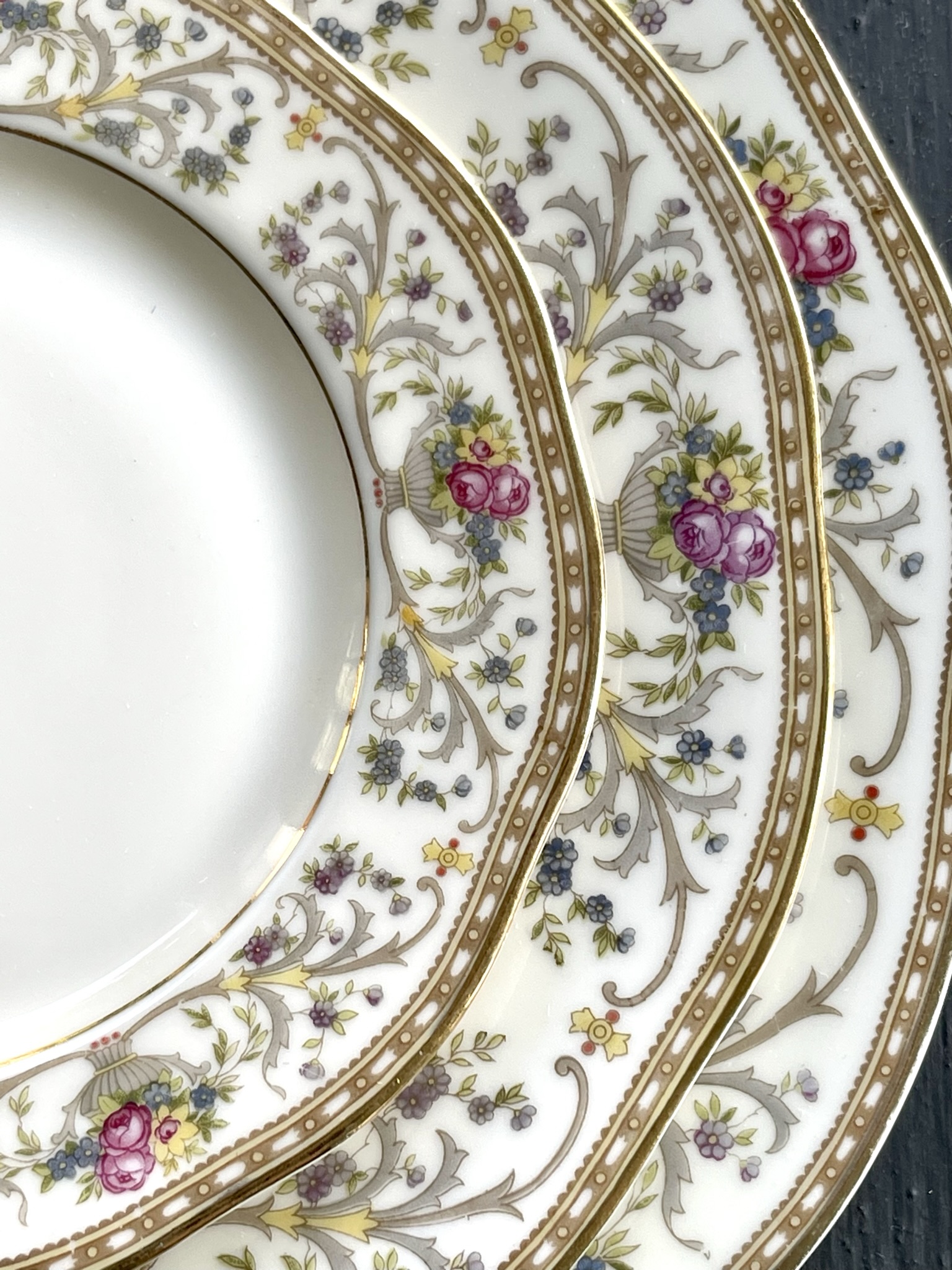 An arabesque pattern with silver-platinum scrollwork and pink rose medallions on white plates — the most cosmopolitan piece in the collection
