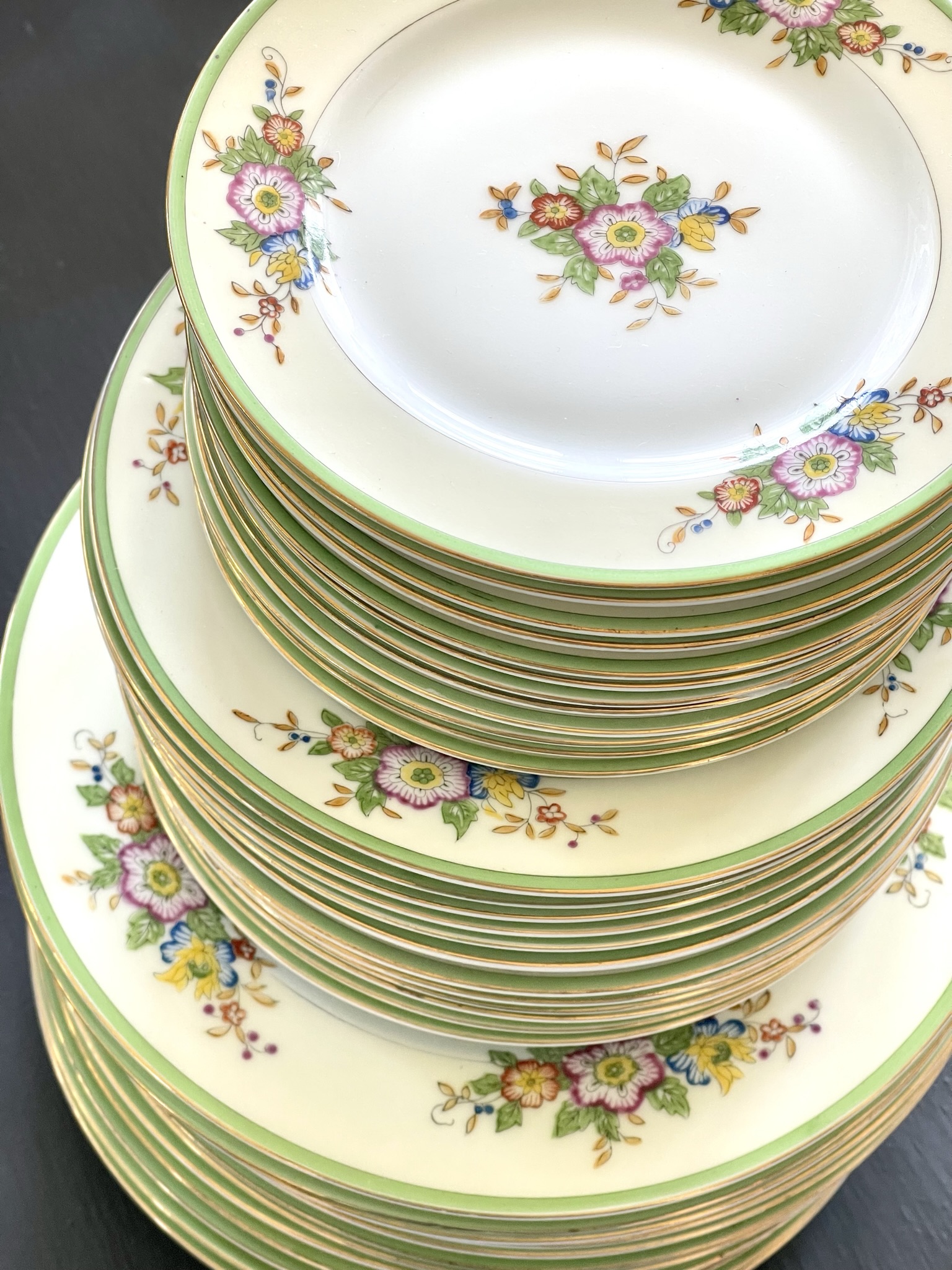 A large Japanese export set — cream ground with green edge band, more than thirty pieces in three sizes stacked, showing the repeating pattern cascading down the stack