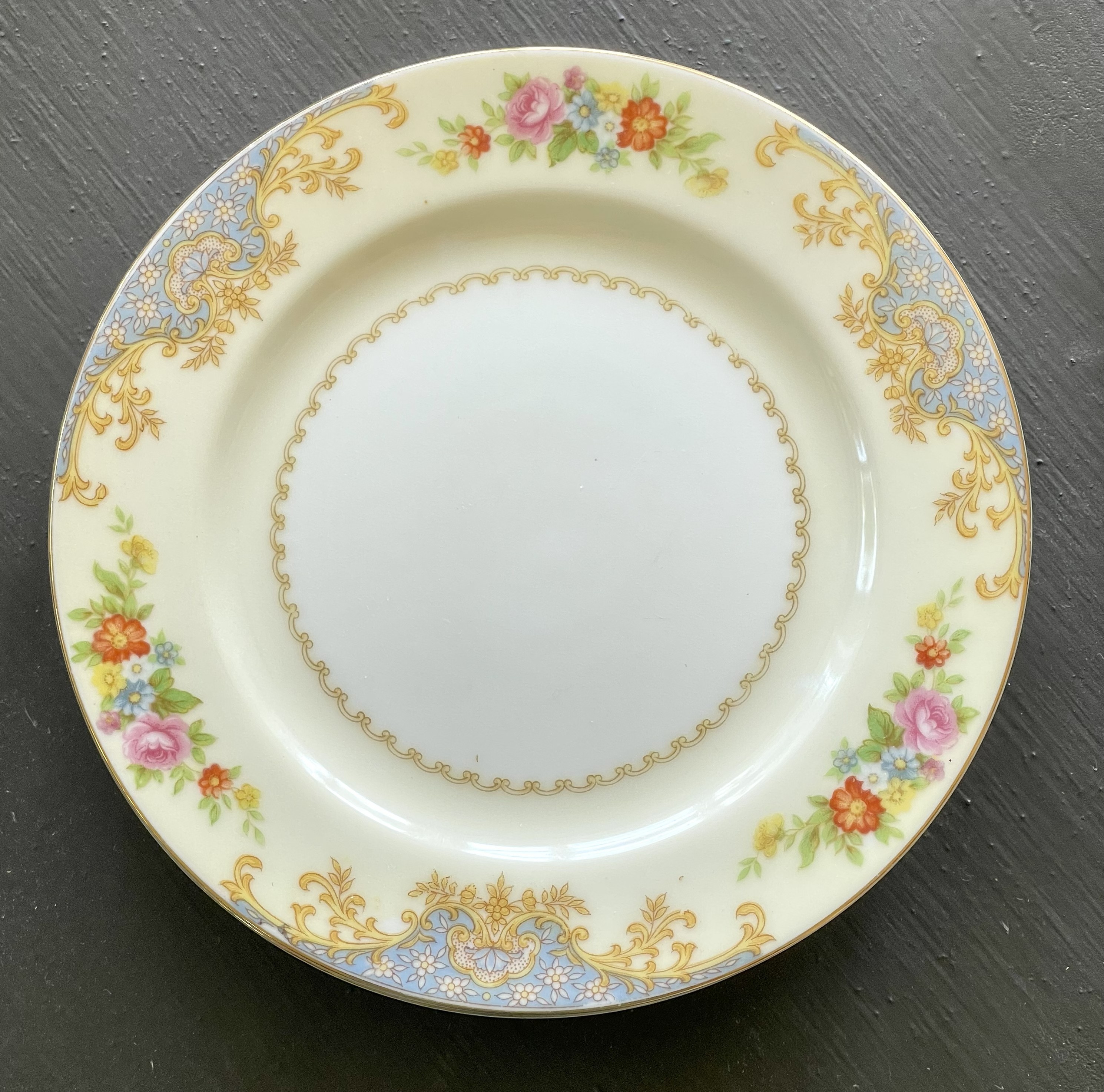 A single formal plate — cream ground, gold rococo scrollwork, blue enamel cartouches at four compass points, hand-painted rose and mixed flower bouquets