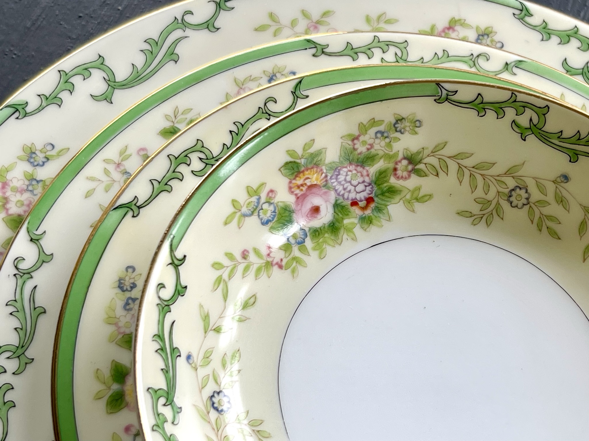 Green acanthus scrollwork set — a close view of the living vine border curling around pink roses and soft lavender flowers on a cream ground