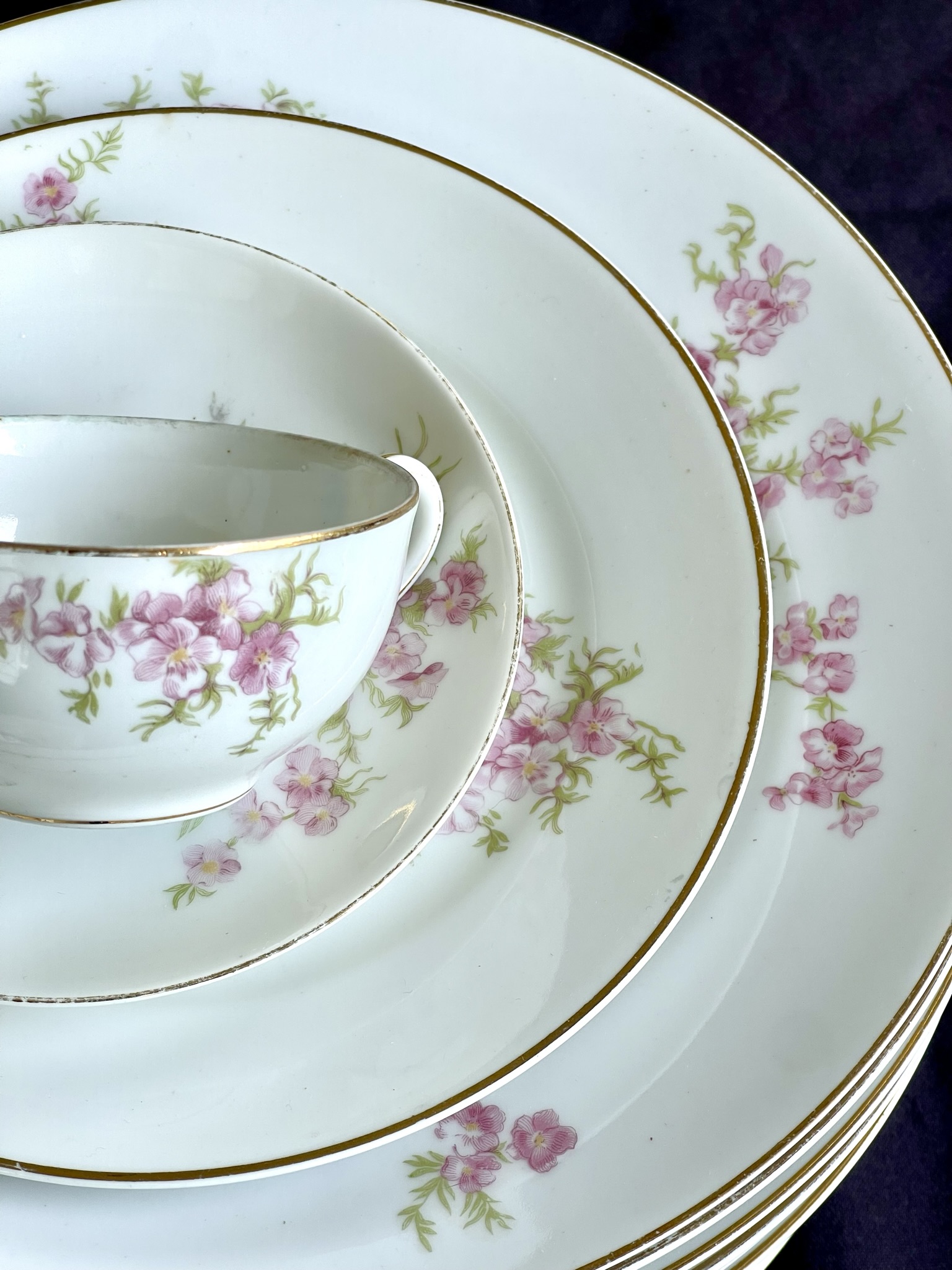 A minimal cherry blossom pattern — scattered pink blossoms on pure white with a worn gold rim, shown with cup, saucer and plates