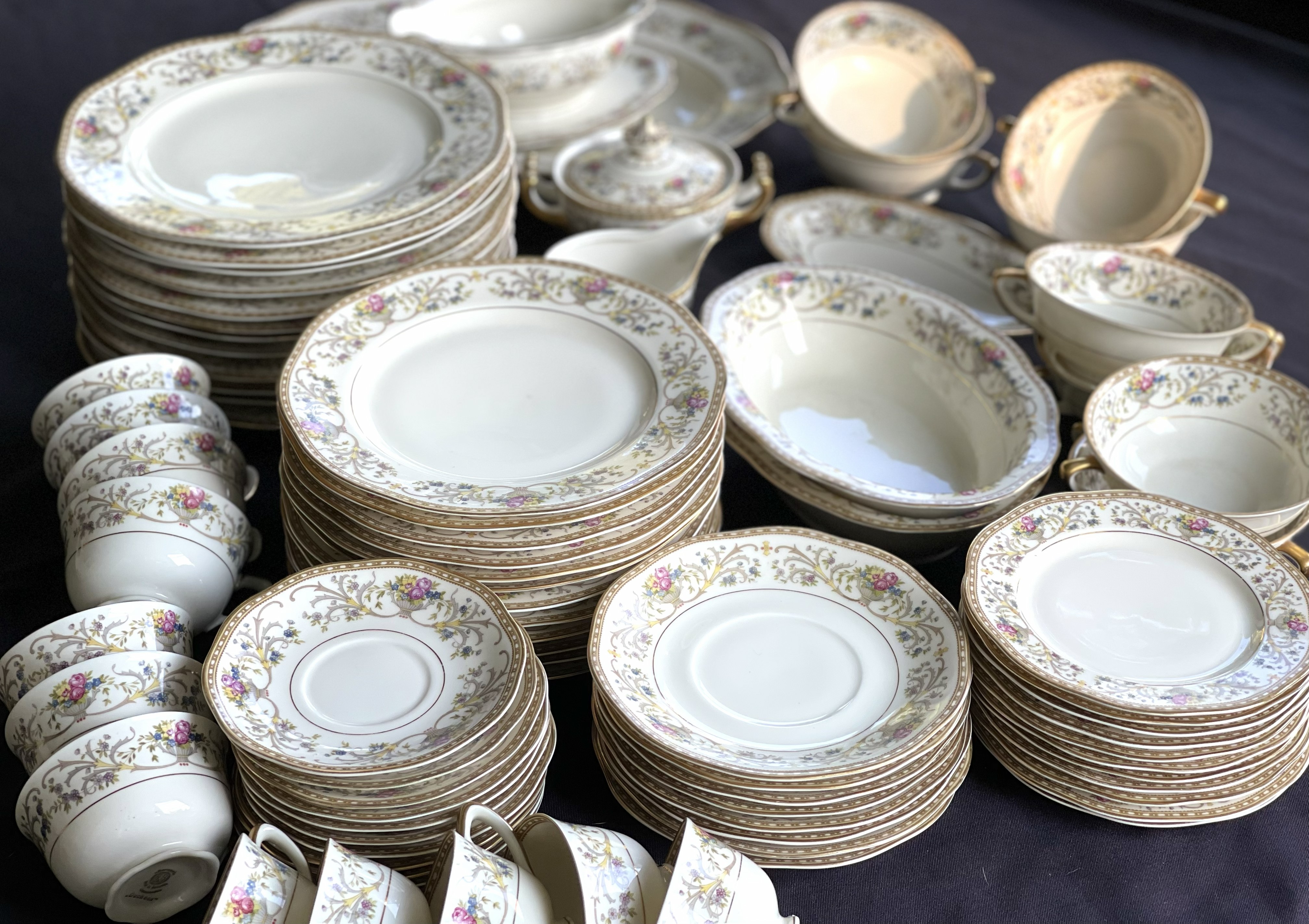 A complete formal china service for twelve laid out in full — dinner plates, salad plates, bread plates, saucers, cups, soup bowls, serving bowls, and a tureen, all in the same gold rococo and floral pattern
