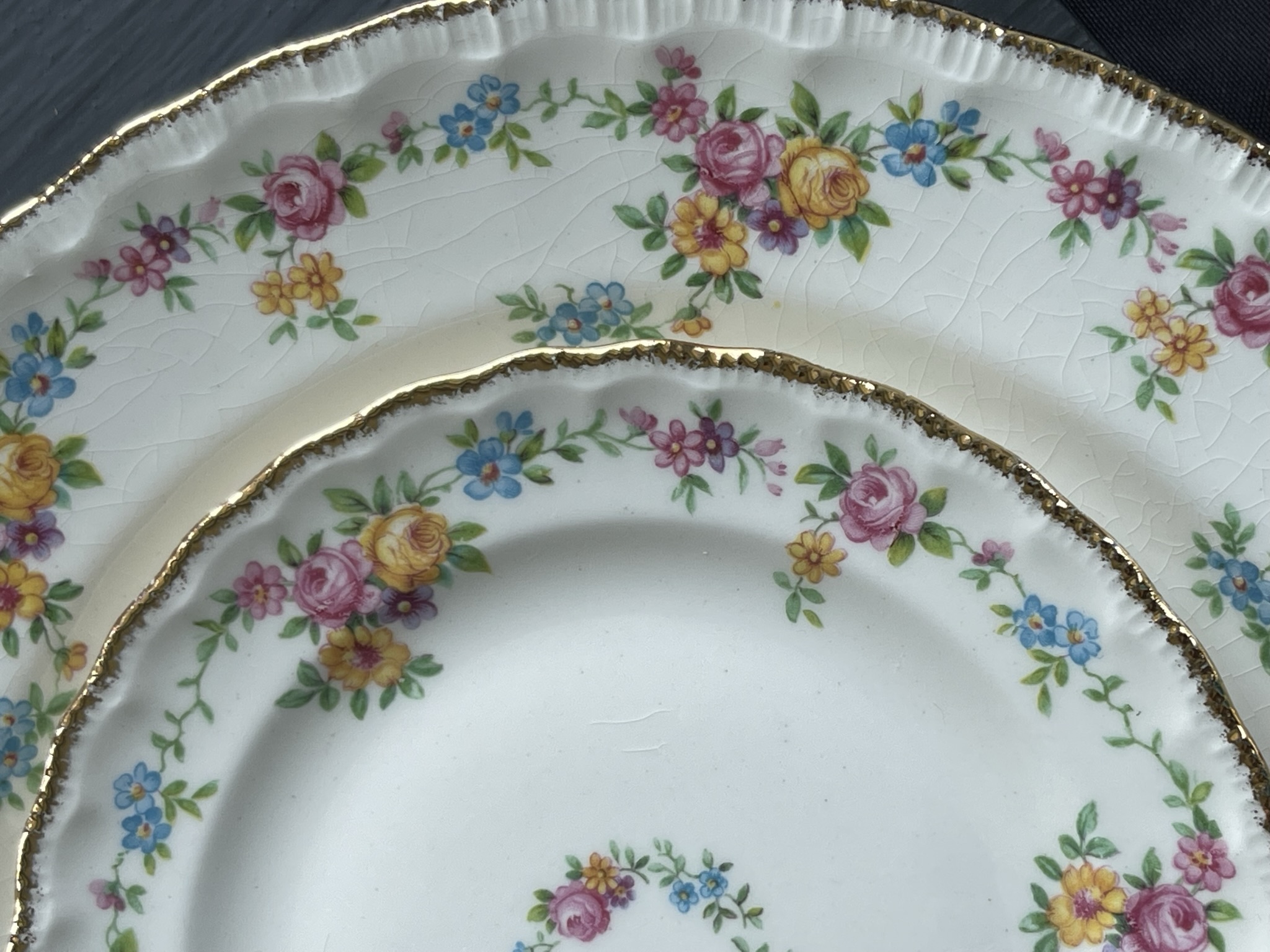 English earthenware with dense all-over pattern of pink roses, yellow roses and blue forget-me-nots, showing rich crazing and a scalloped edge with worn gold