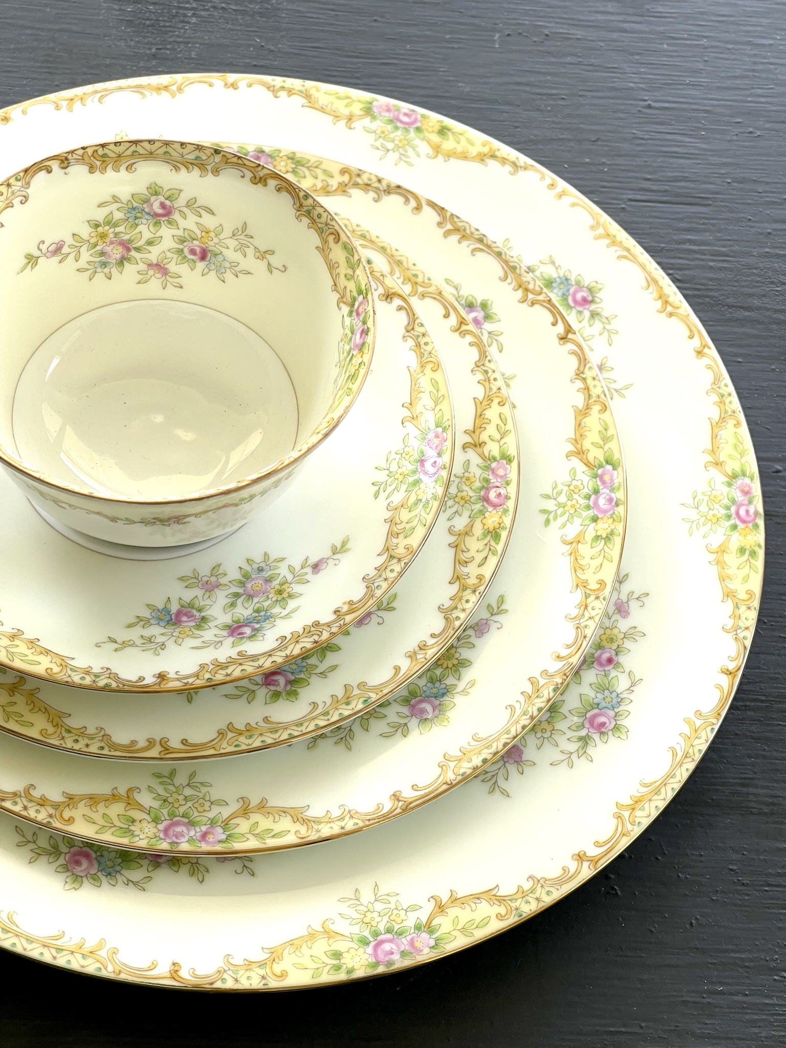 A warm golden rococo pattern with cream-yellow ground, gold cartouches, and pink roses with blue forget-me-nots on nested plates and bowl