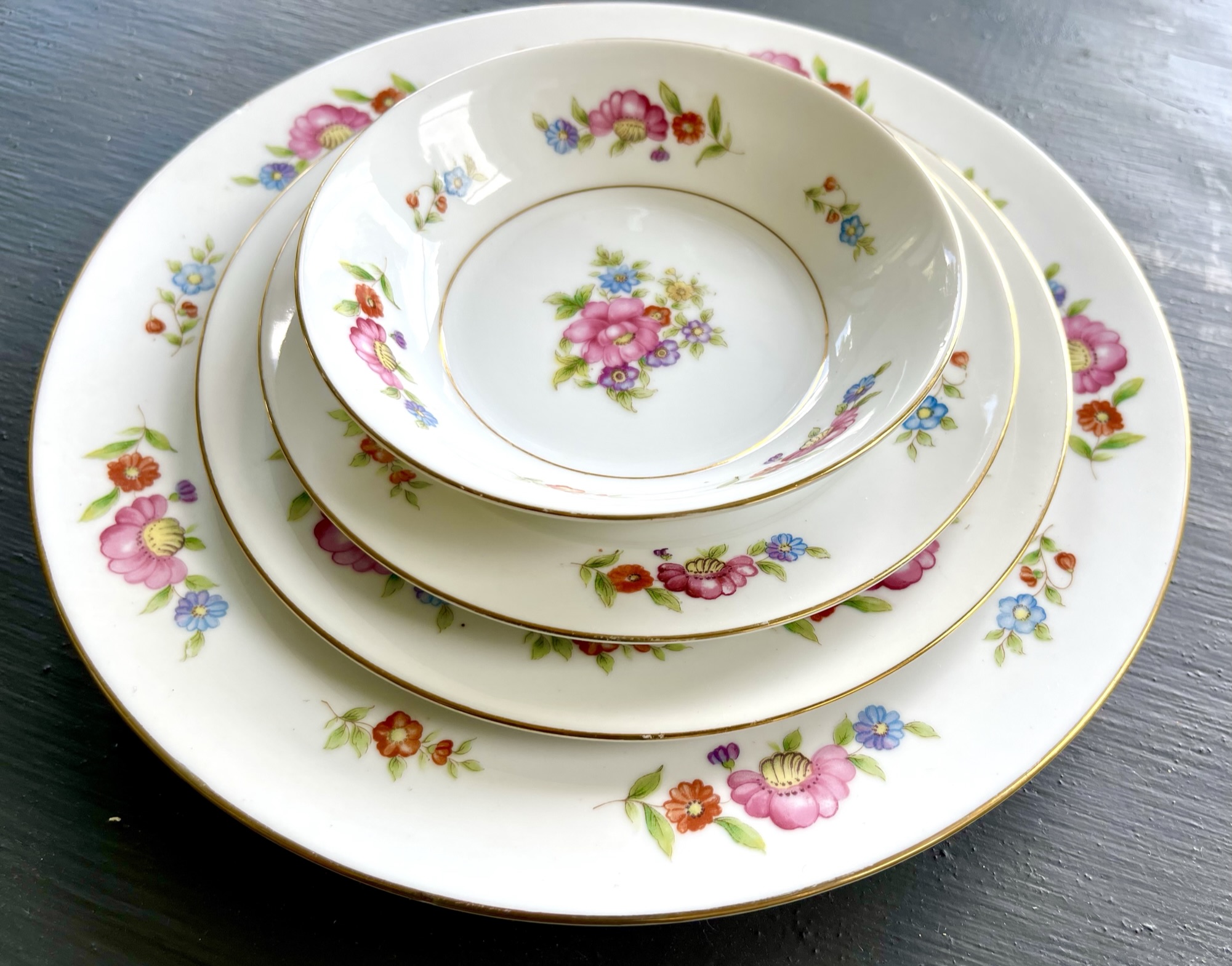 A Meito export pattern with scattered pink, red, orange and blue flowers across white plates, with a small center bouquet in a nested bowl