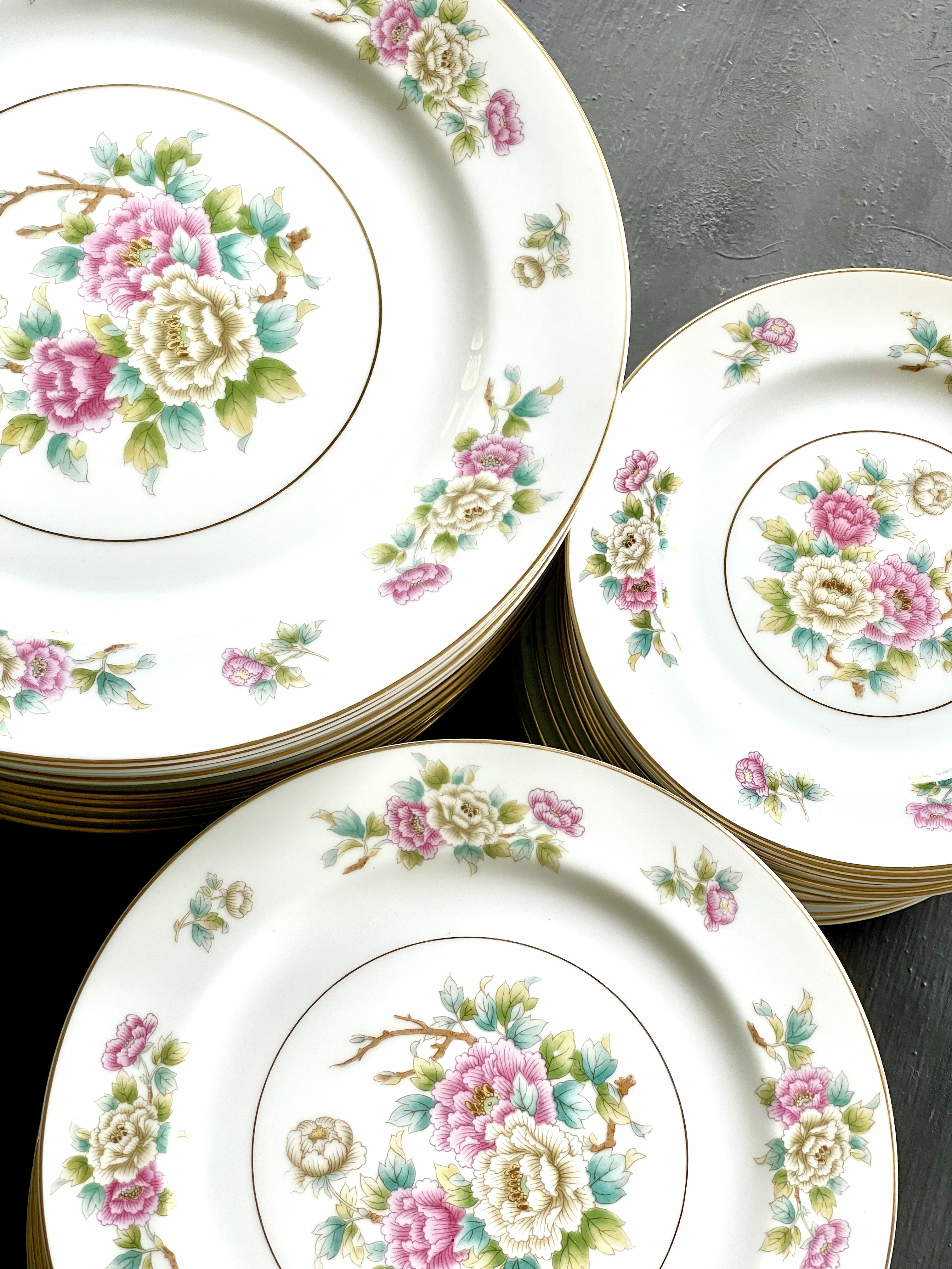Three stacks of the peony set — dinner plates, salad plates, and bread plates all in the same pattern, pink and cream peonies on white, the full scale of the service visible
