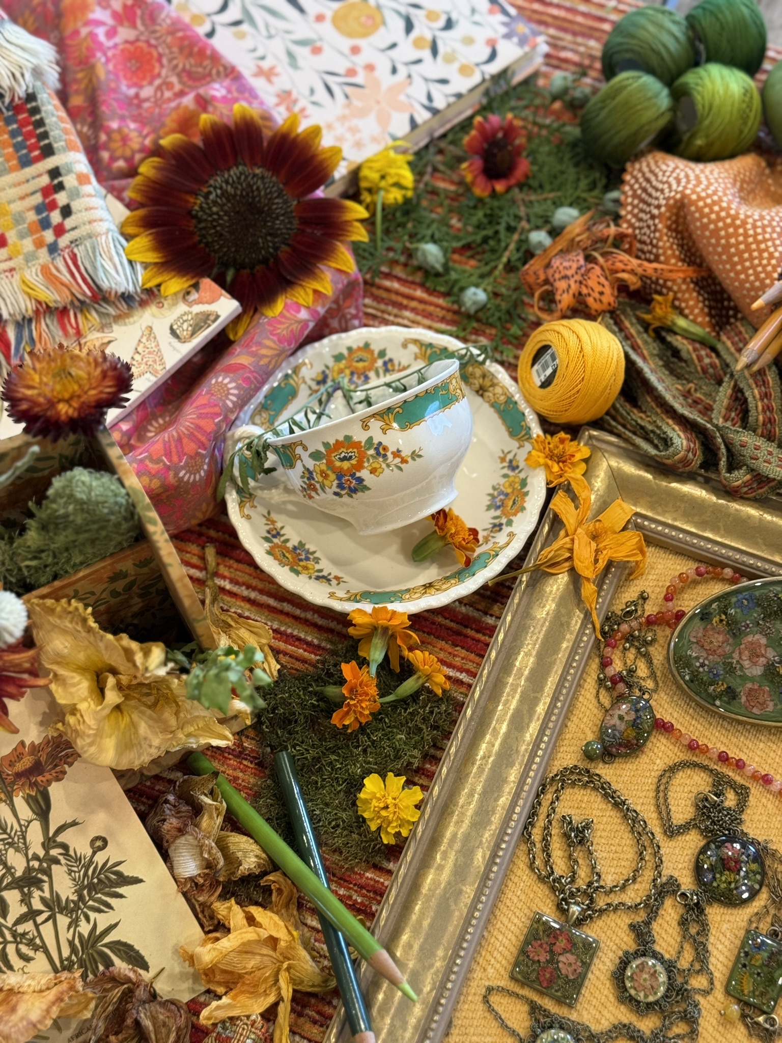 A teal-and-gold floral cup and saucer in a collector's still life with sunflowers, marigolds, jewelry and vintage frames