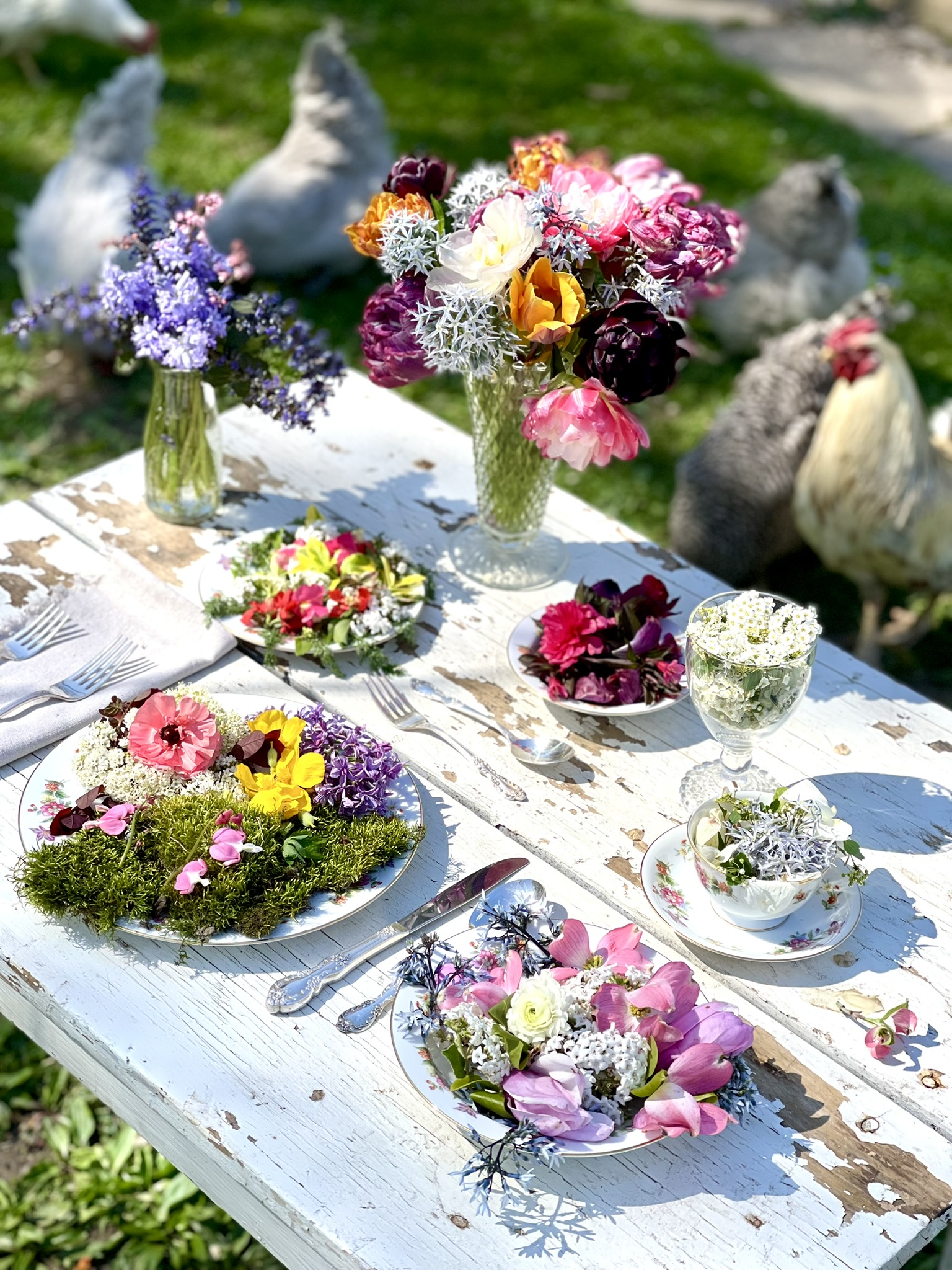 Two white geese at the edge of the table, china plates filled with flowers in the foreground