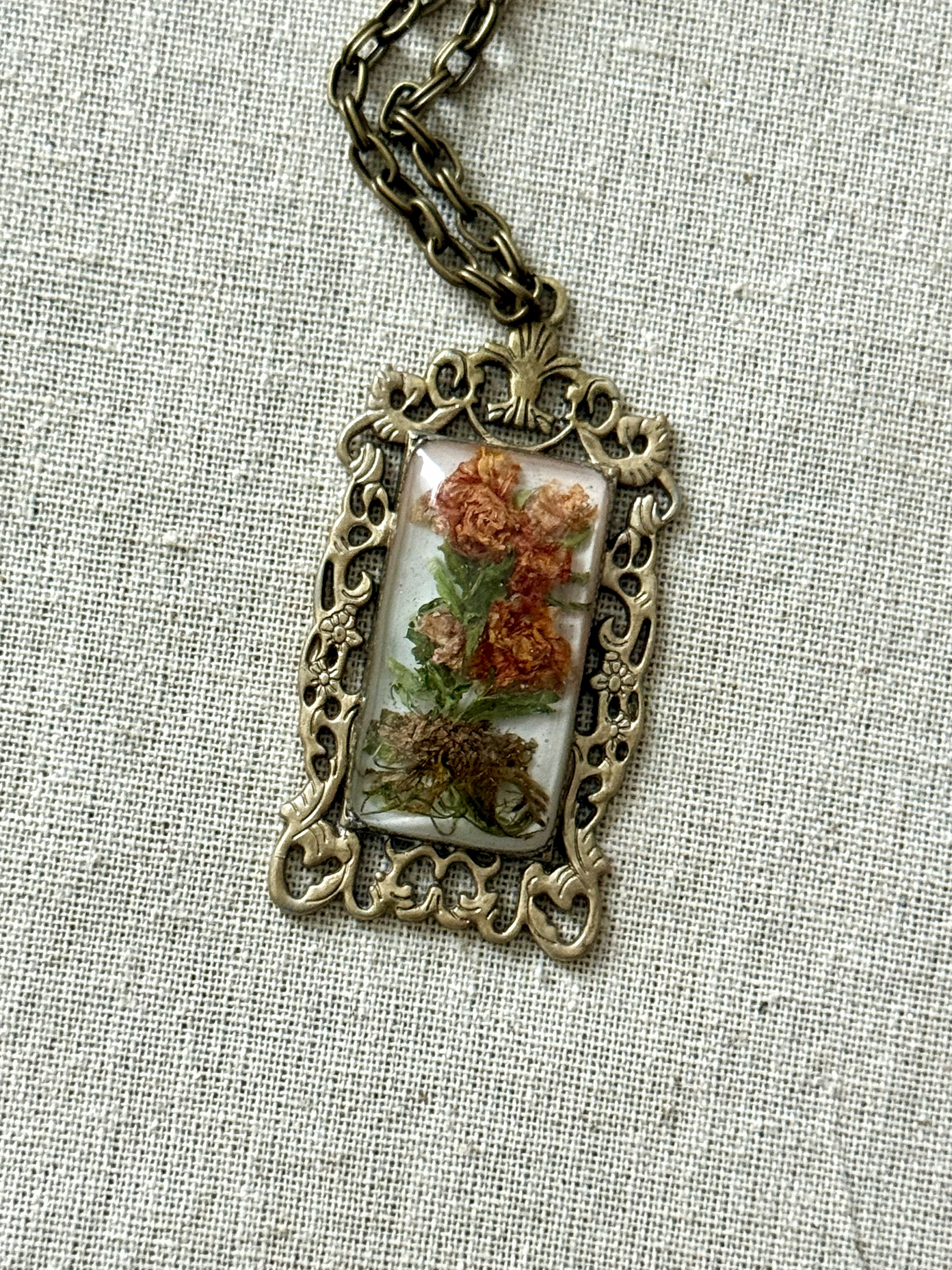 Rectangular brass filigree pendant with dehydrated lily-roses on linen