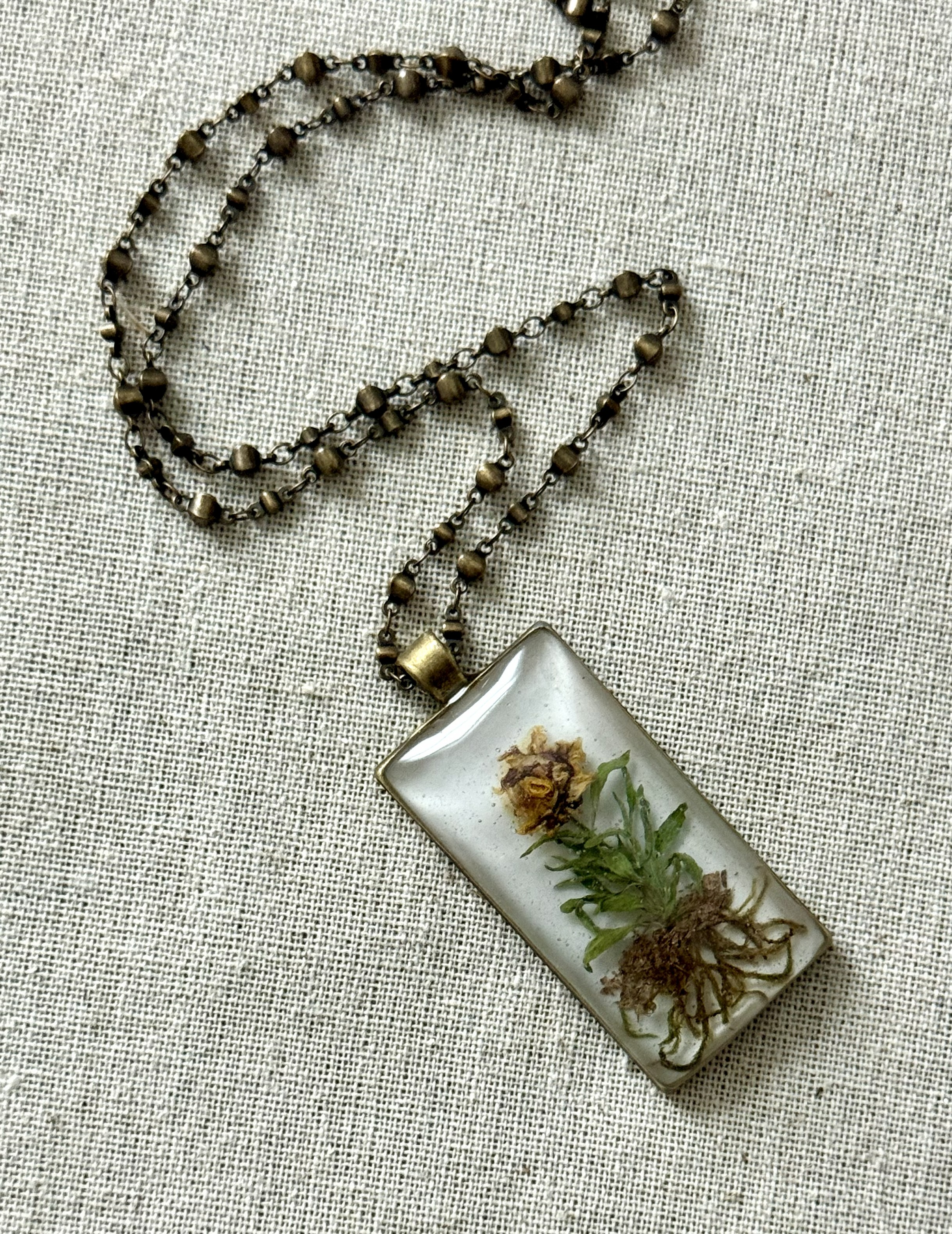 Rectangular pendant on beaded brass chain, single lily-rose arrangement with greenery