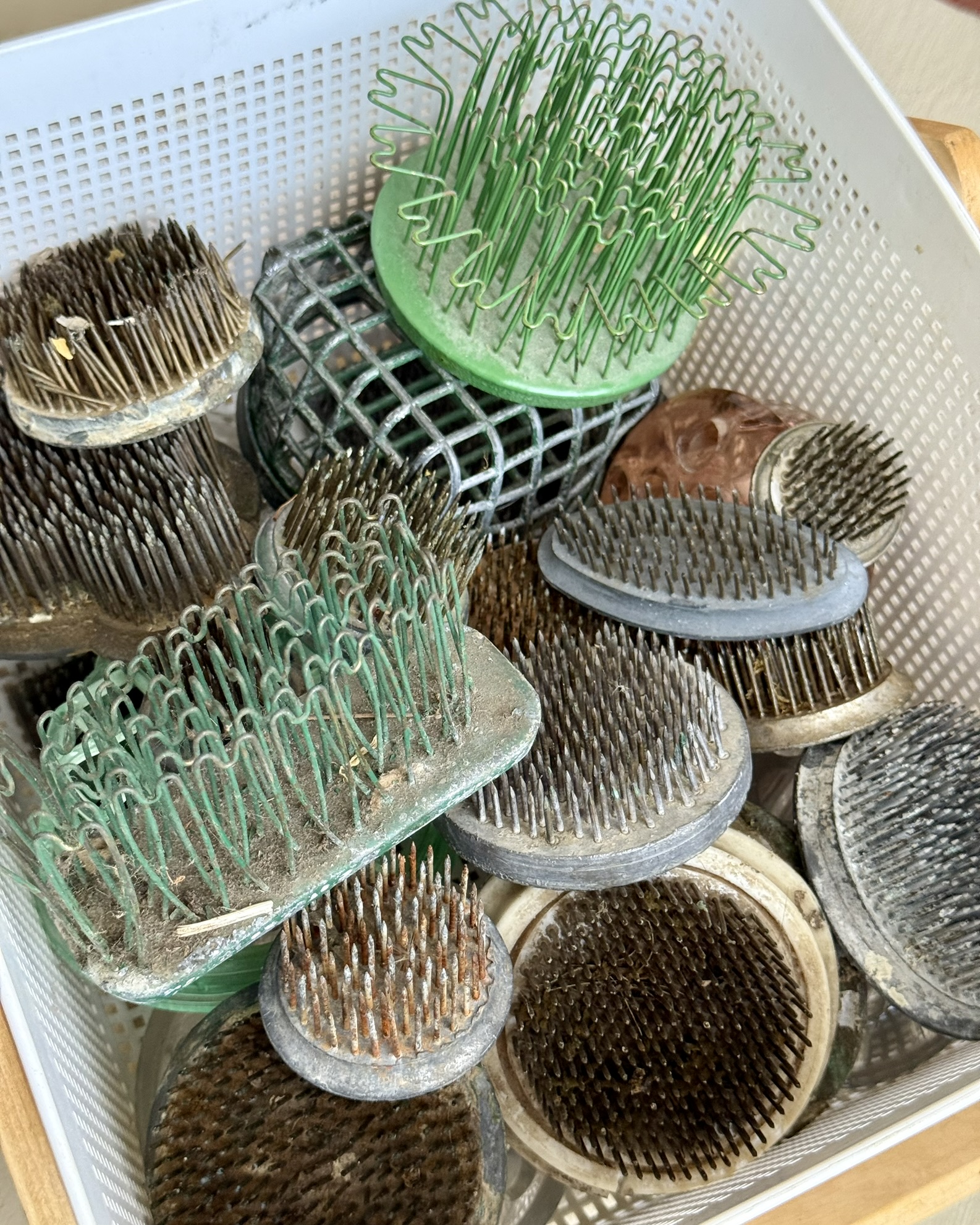 A white basket filled with vintage kenzans, wire grids, dome frogs and cage frogs — the working collection