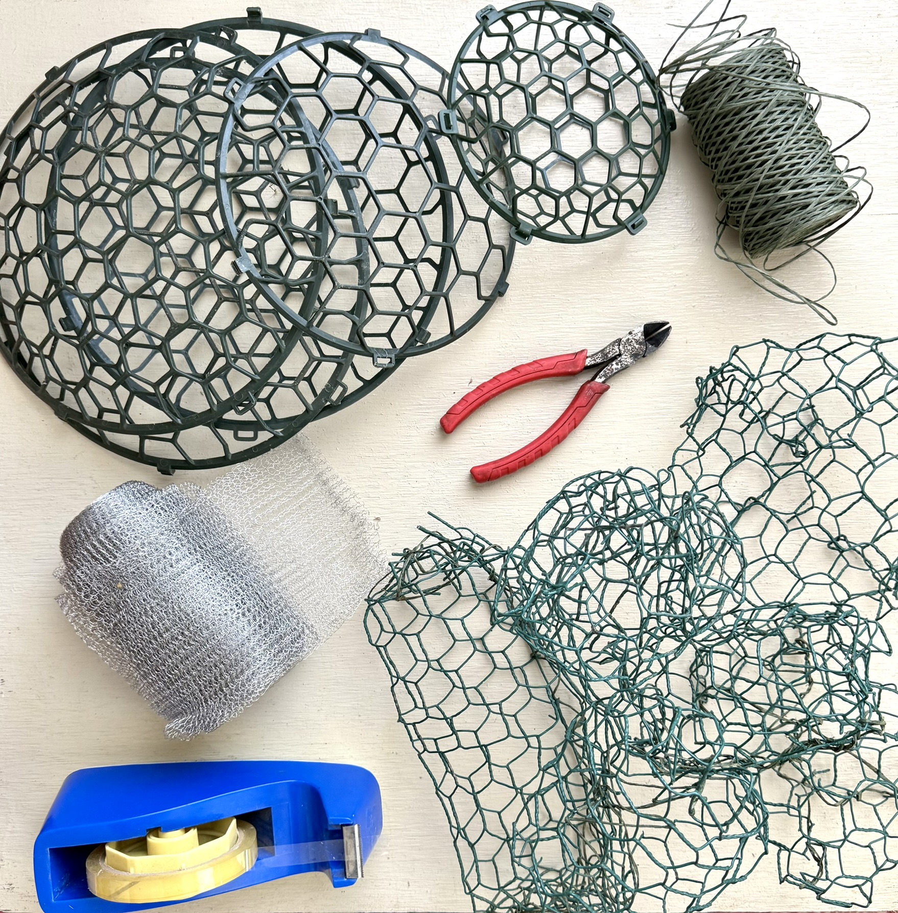 Wire dome frogs in four sizes, steel wool, crumpled chicken wire, red pliers, sage wire, blue tape — the dome and cage toolkit