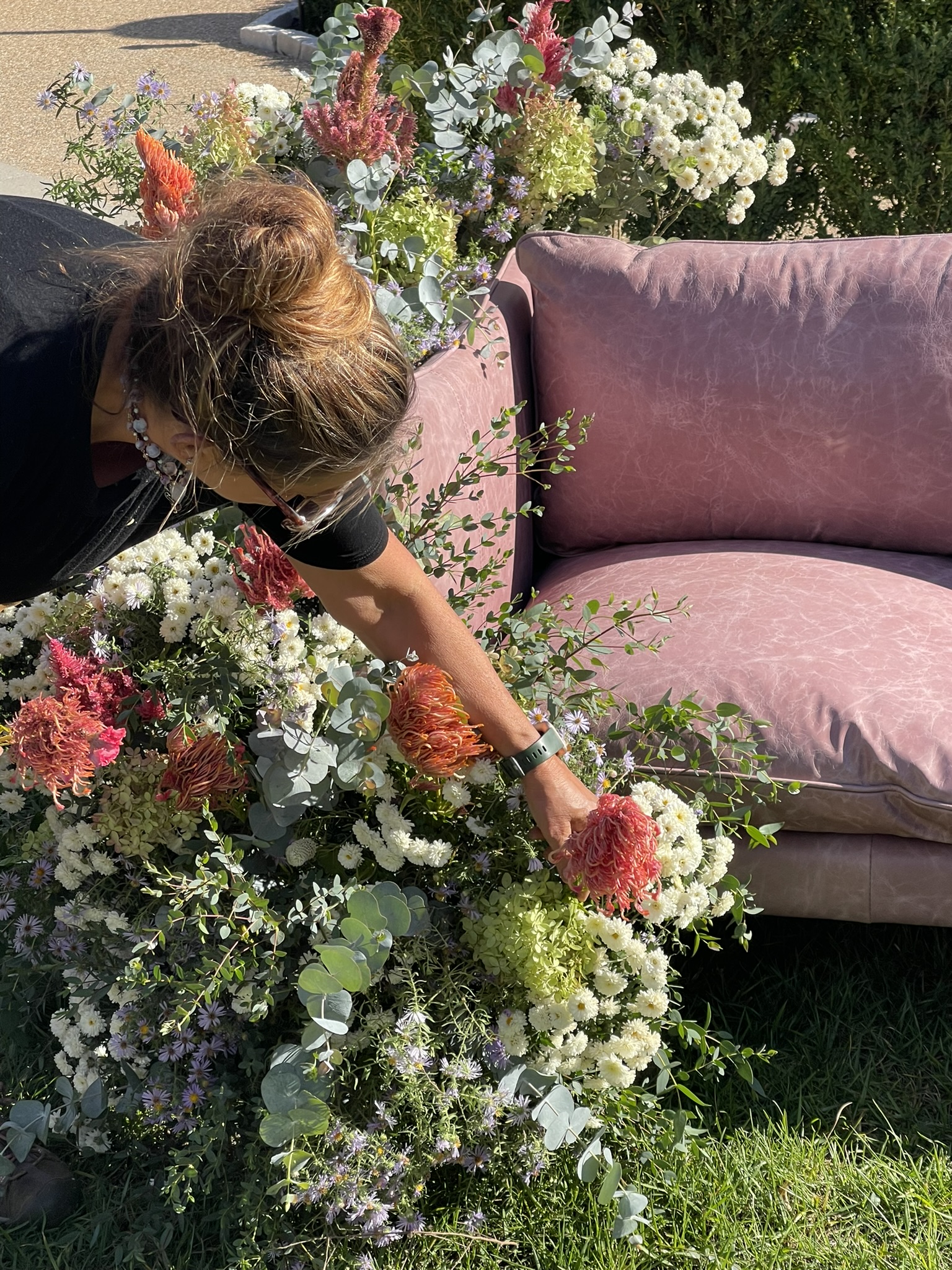 Overhead close: Luli deep inside the armature, placing a pincushion protea by hand