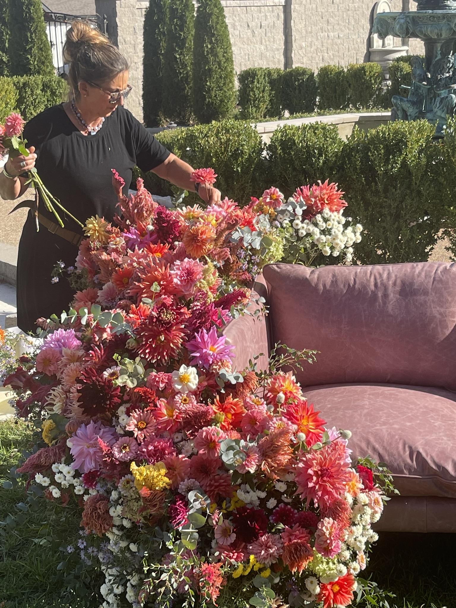 Luli building the dahlia armature — pink, coral and red dahlias rising from the sofa frame, mid-build