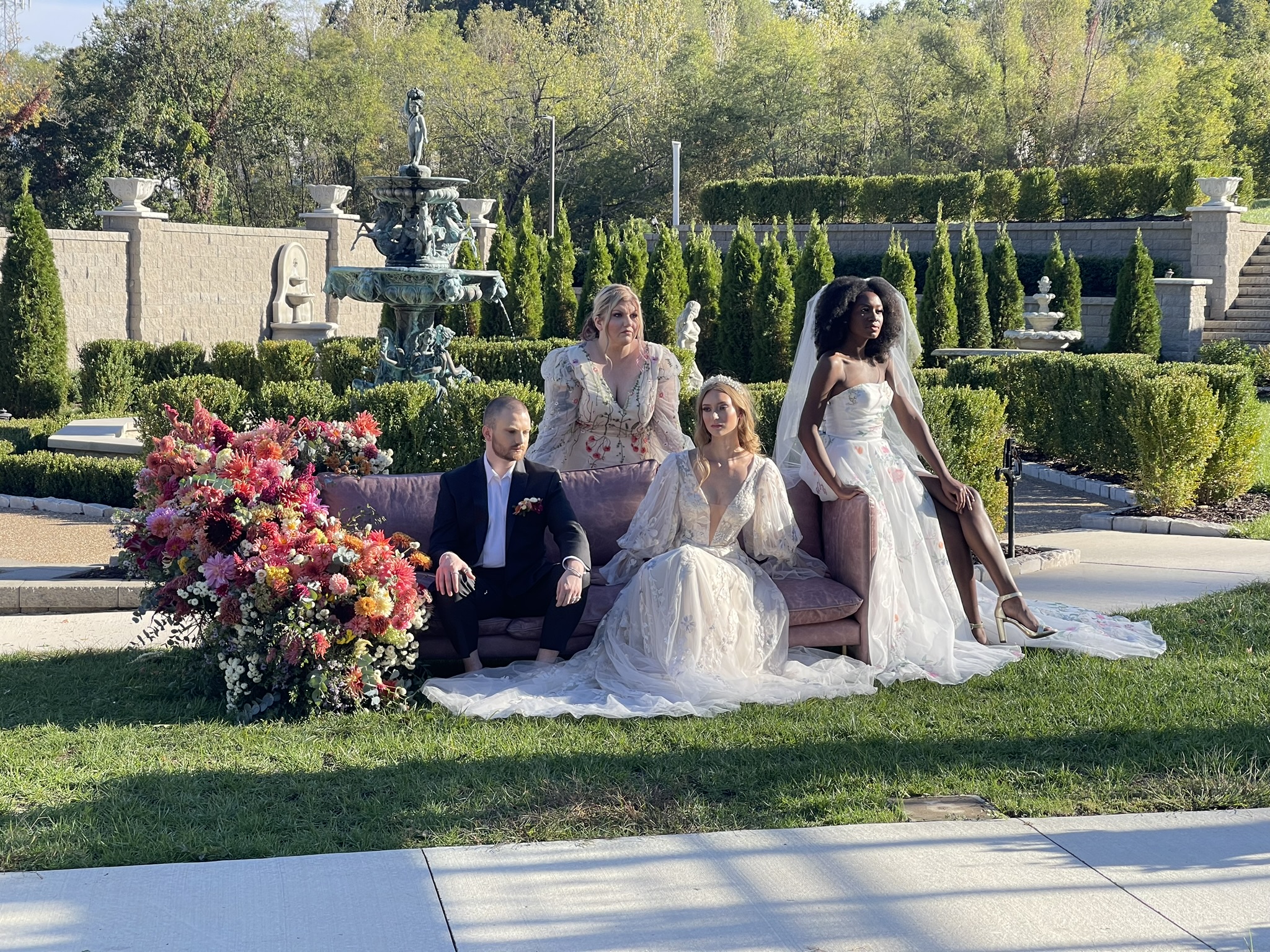 The finished editorial: models on the mauve sofa in the formal garden — the dahlia armature to the left. Saint Louis Bride.