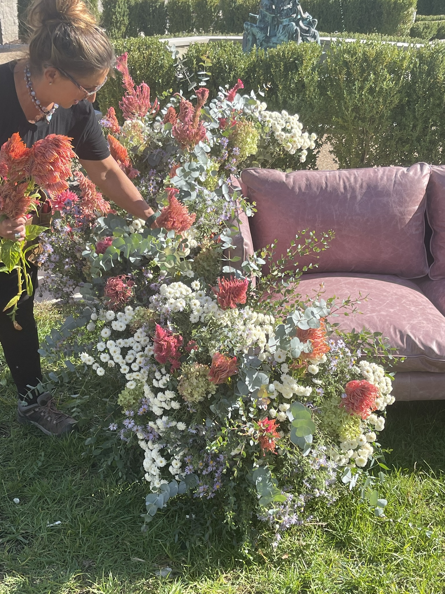Luli building the white and celosia sofa armature — asters, pincushion protea and eucalyptus