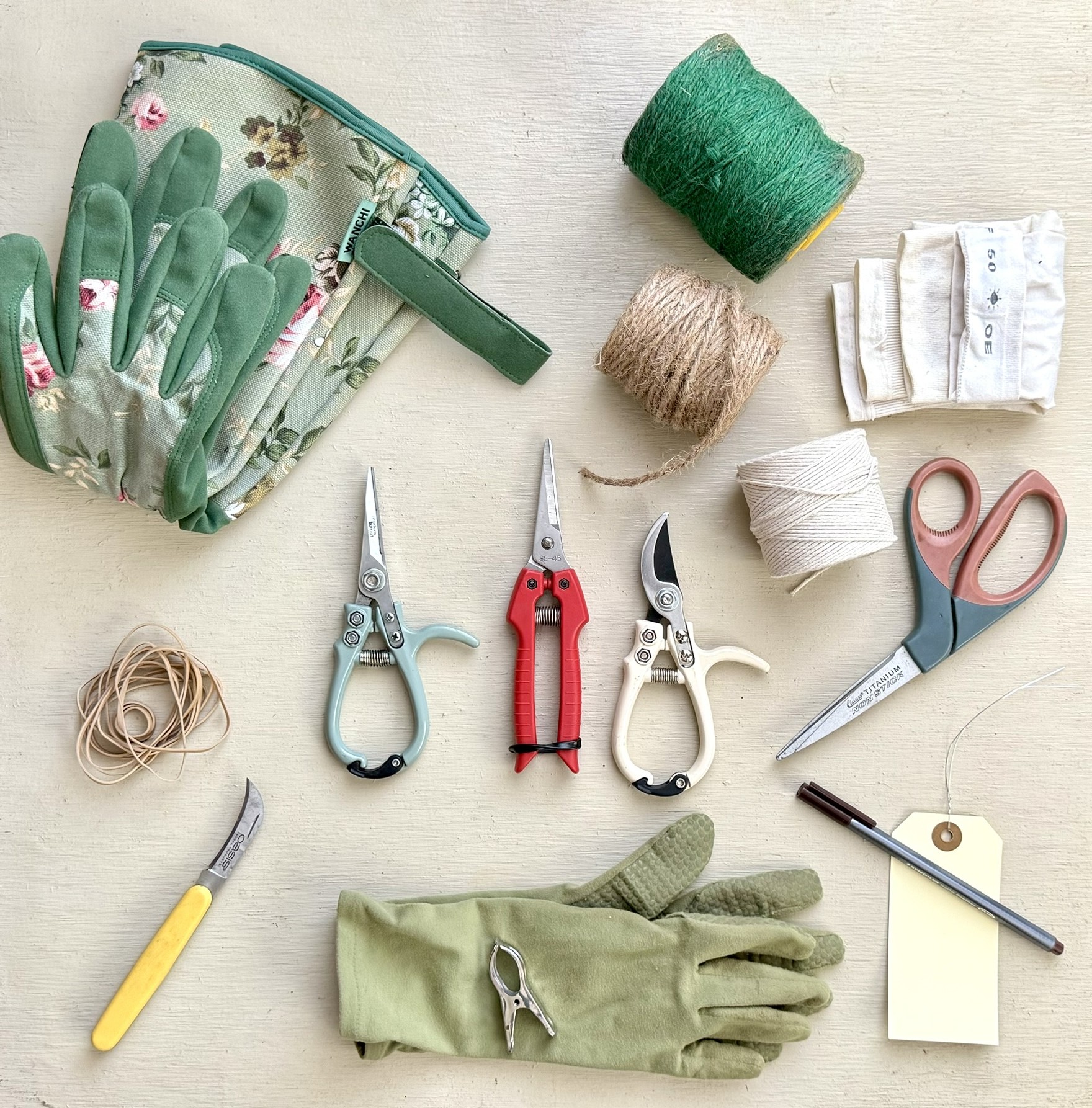 The full kit laid flat: floral-print gloves, jute twine, cotton twine, green twine, three types of snips, OASIS knife, rubber bands, garden gloves, price tag and pen