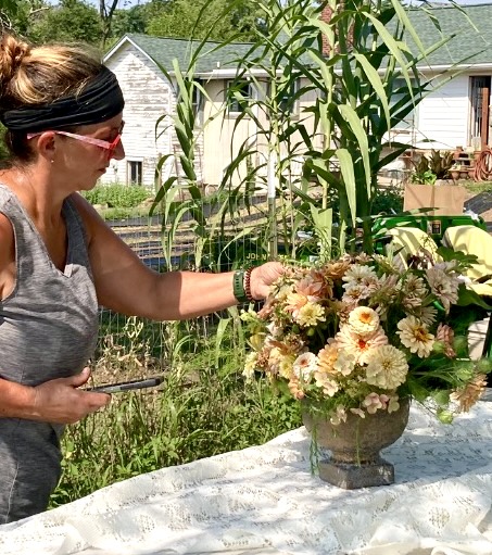 Outdoor step ladder staging area with zinnias in white bucket at top, red snips, mason jar arrangement on middle shelf — field harvest setup