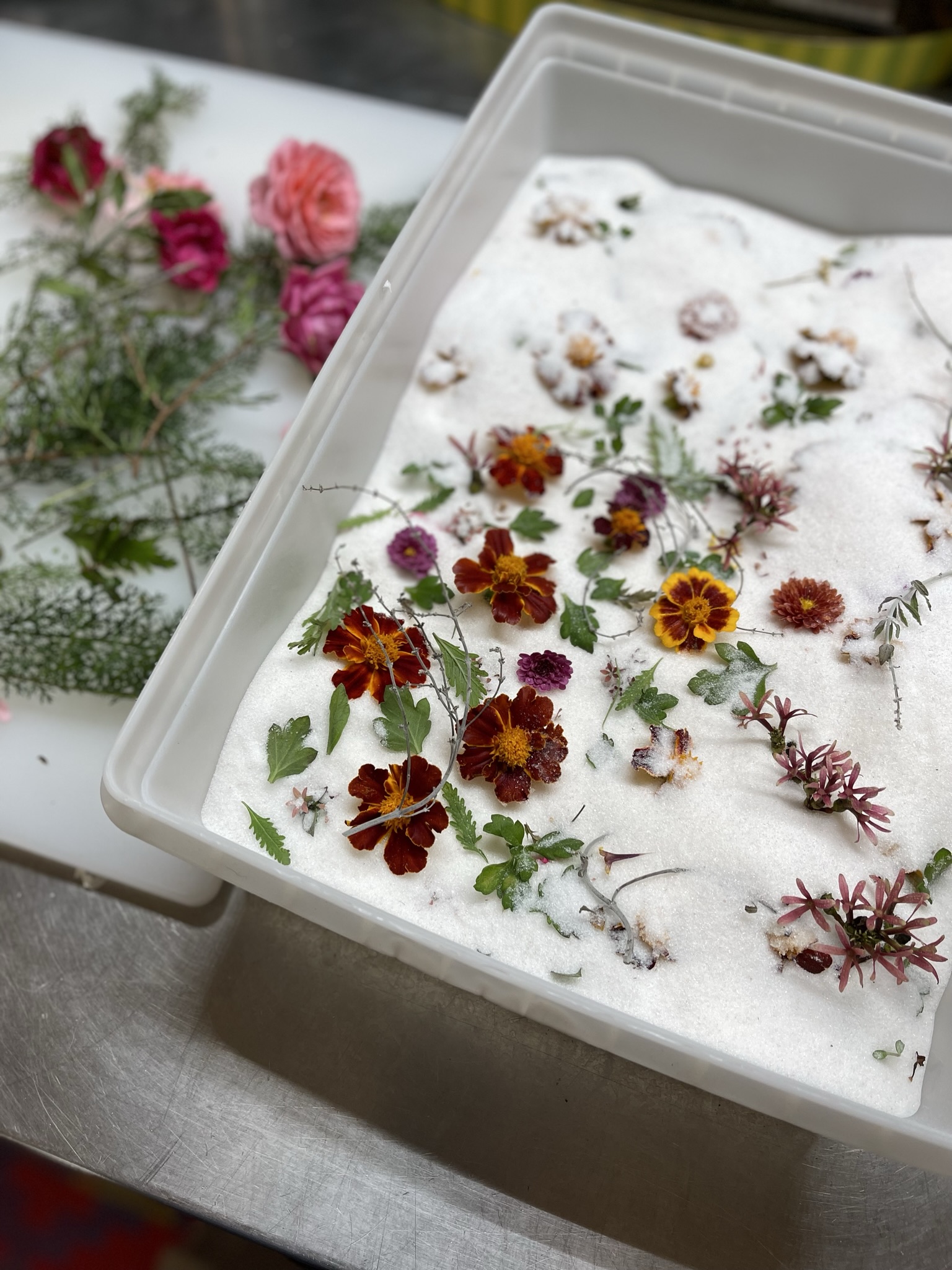 Marigolds and small flowers arranged on a silica tray alongside roses waiting to be processed
