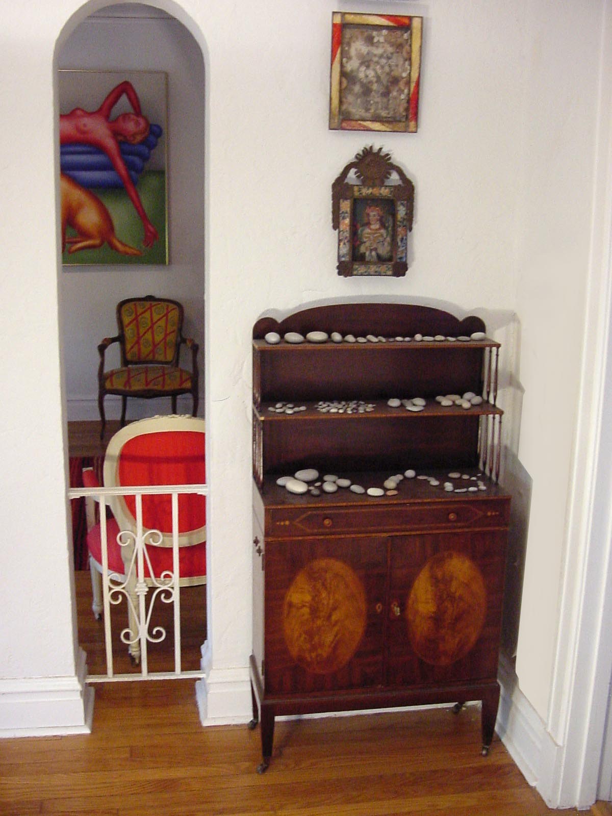 Her apartment — the antique mahogany shelving unit lined with stones in careful arrangements, bold artwork visible through an arched doorway