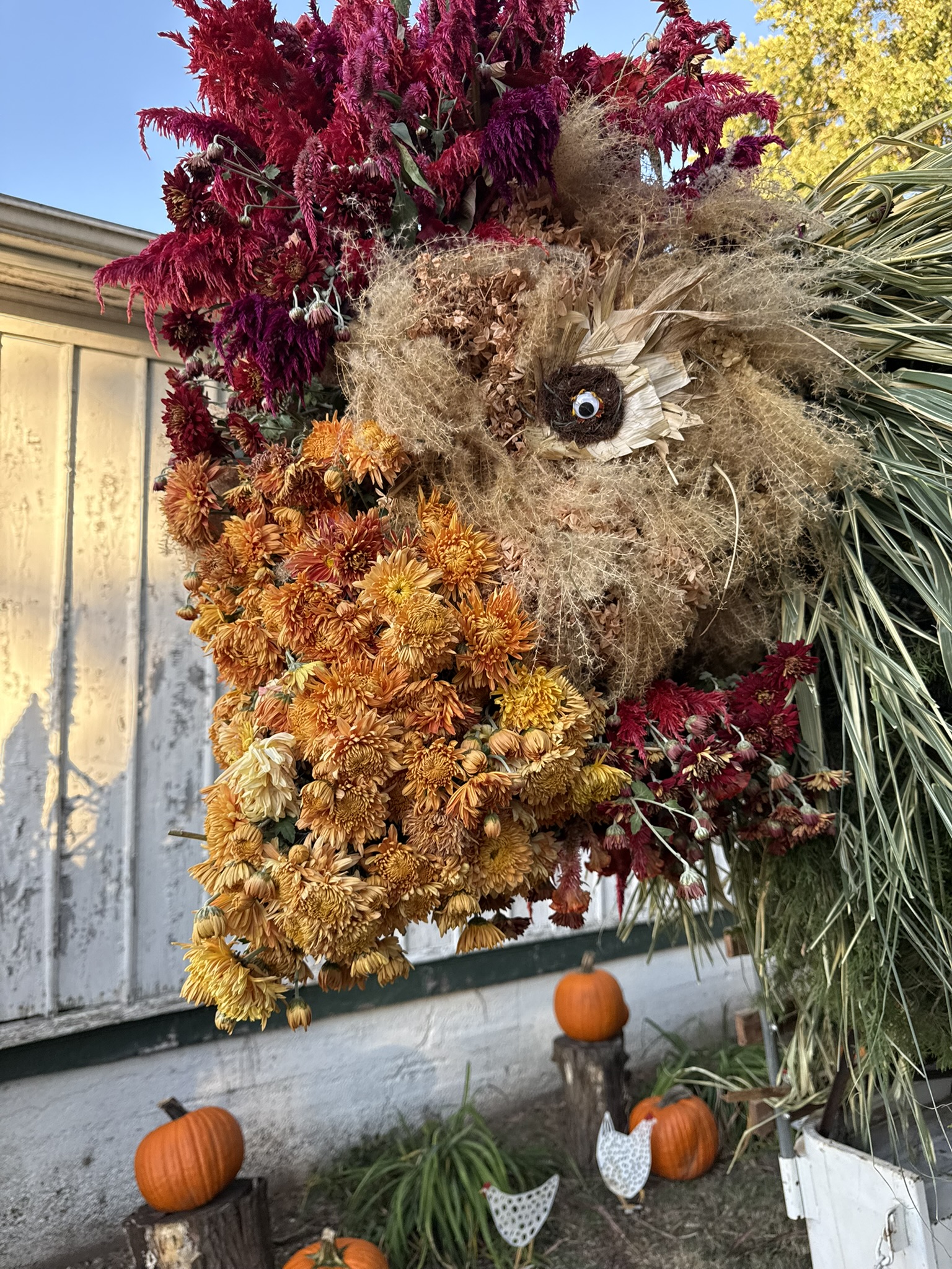 Close-up of the rooster's wattle — layers of orange and gold mums cascading beneath a celosia crown in crimson and magenta
