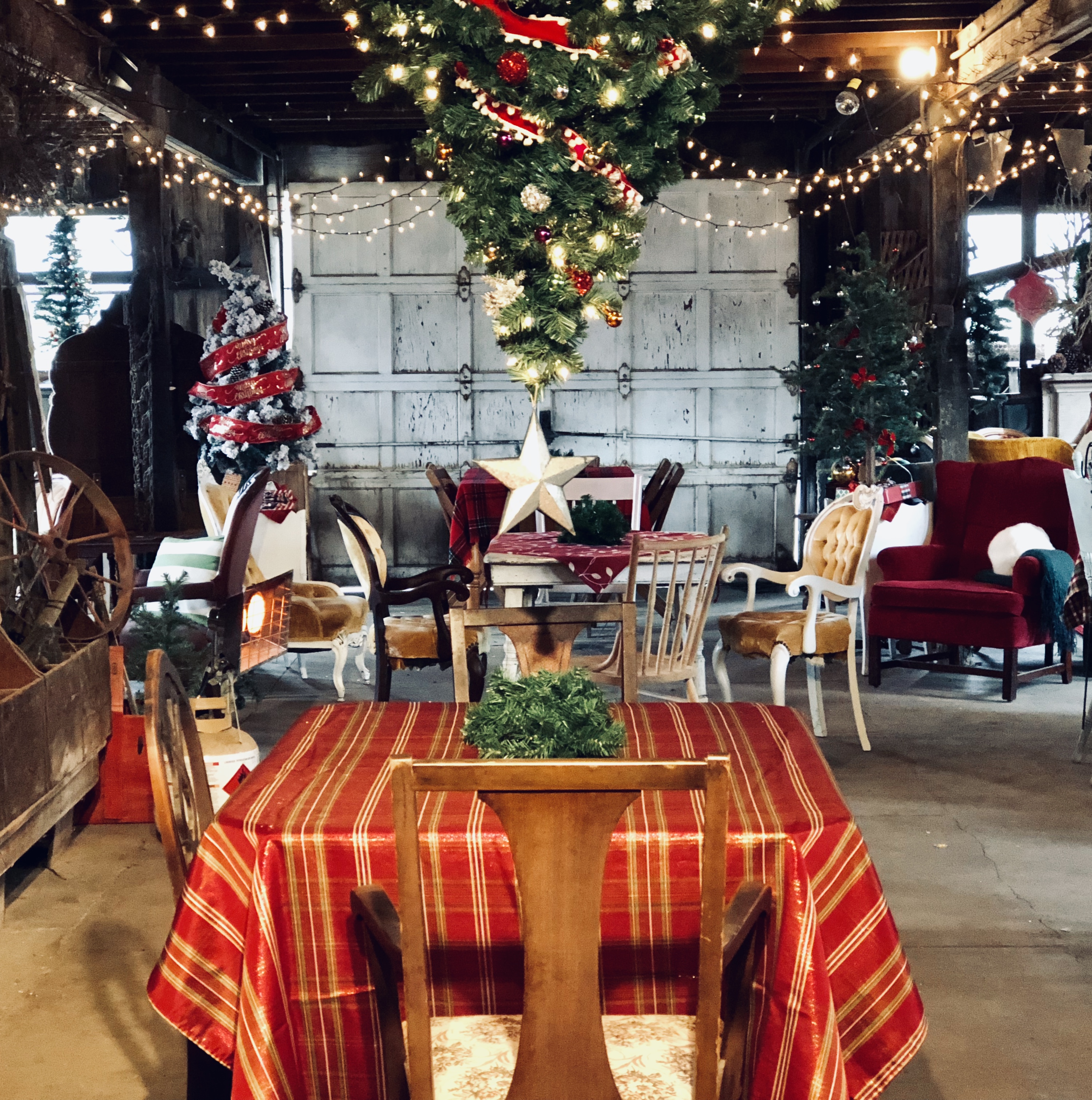 Barn interior dressed for the holiday party — string lights, upside-down tree hanging from the rafters, plaid tablecloths on mismatched vintage furniture
