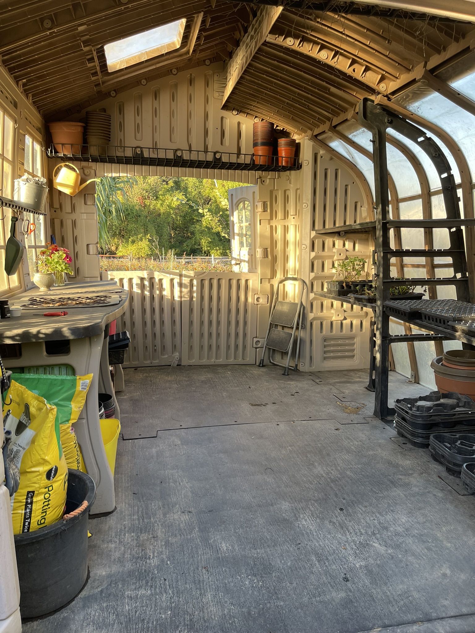 Interior of the garden studio being emptied at season's end — golden afternoon light through the window, terra cotta pots stacked on shelves, bench cleared