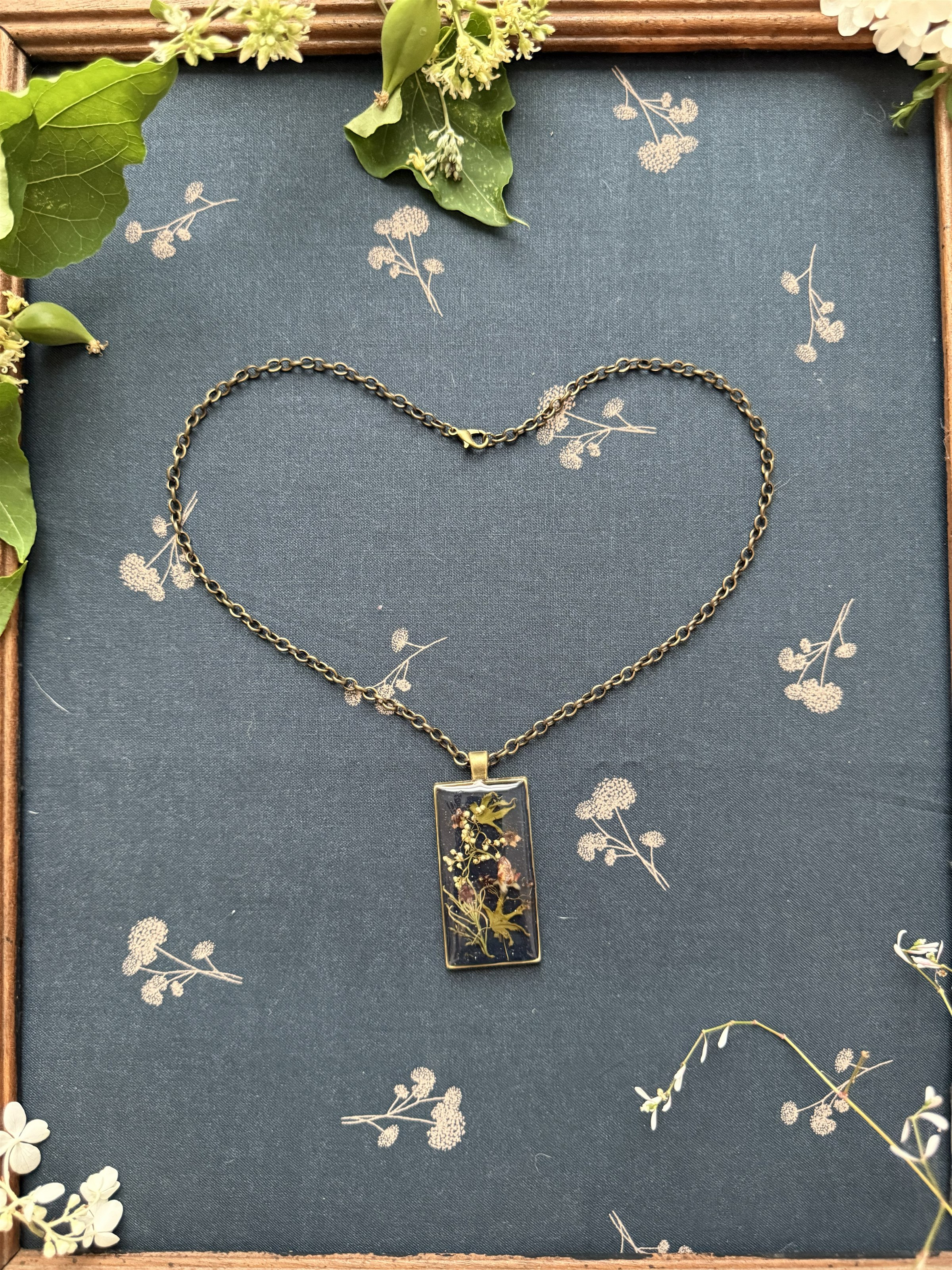 A single dark botanical pendant on a chain arranged as a heart on deep blue fabric
